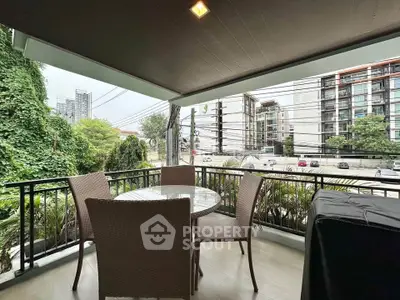 Spacious balcony with outdoor seating and lush greenery view in urban setting.