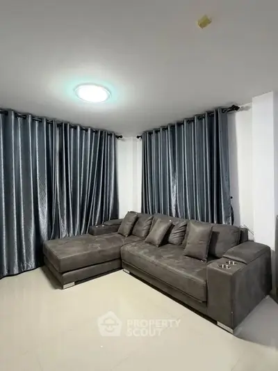 Modern living room with sleek gray sectional sofa and elegant floor-to-ceiling curtains.