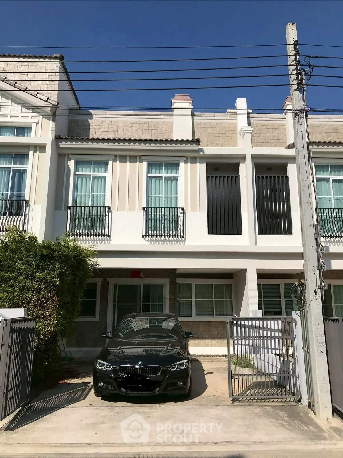 Modern townhouse exterior with driveway and parked car under clear blue sky.