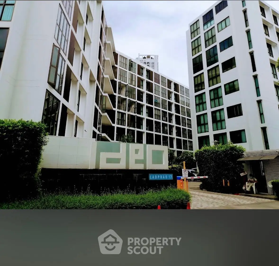 Modern condominium building with sleek design and lush greenery at entrance.