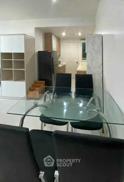 Modern dining area with glass table and sleek kitchen in open layout apartment.