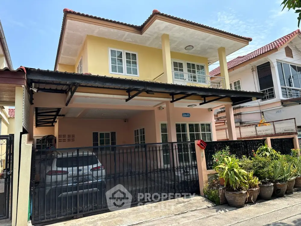 Charming two-story house with gated driveway and lush potted plants in a serene neighborhood.