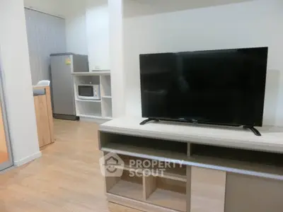 Modern living room with sleek TV stand, microwave, and fridge in a cozy apartment setting.