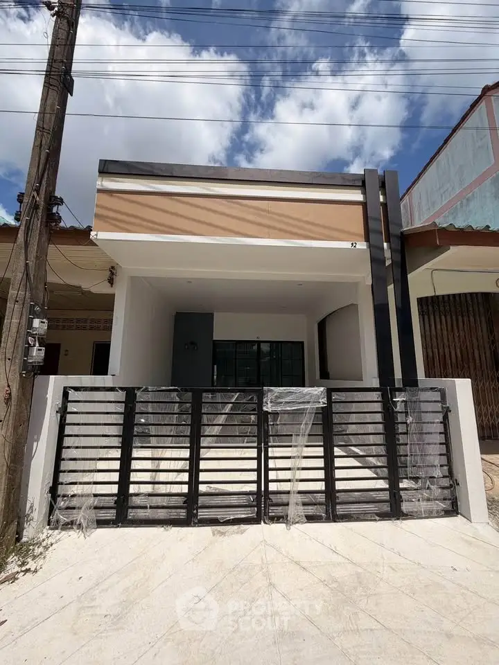 Modern single-story house with sleek black gate and minimalist facade under a clear blue sky.