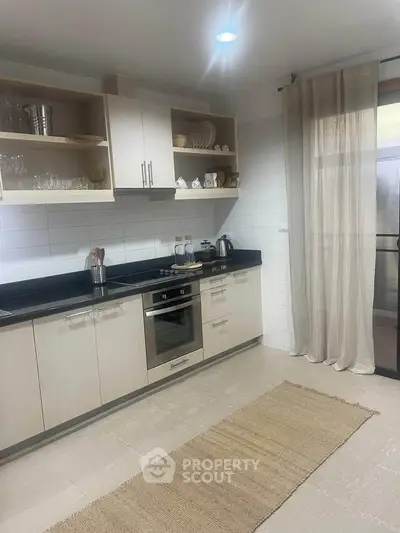 Modern kitchen with sleek cabinetry and built-in oven, featuring open shelving and neutral tones.
