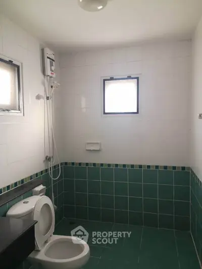 Spacious bathroom with green tiled walls and modern fixtures, offering a clean and bright atmosphere.