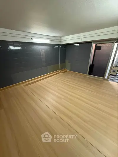 Spacious empty room with wooden flooring and modern tiled walls