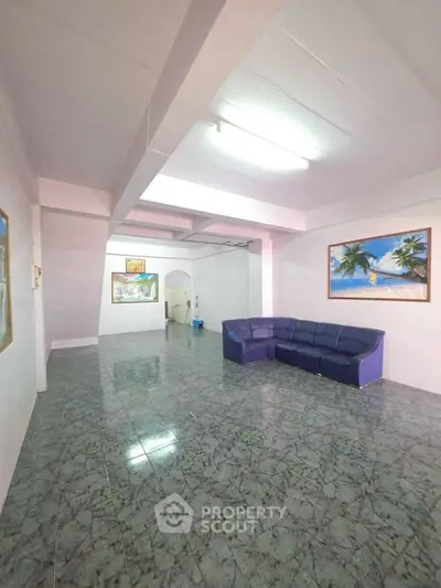 Spacious living room with tiled flooring and modern decor, featuring a comfortable blue sofa and vibrant wall art.