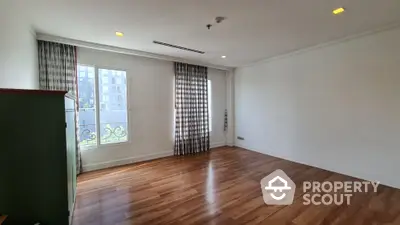 Spacious empty room with hardwood floors and large windows in modern apartment.