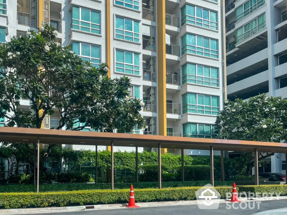 Modern residential building with lush greenery and covered walkway in urban setting.