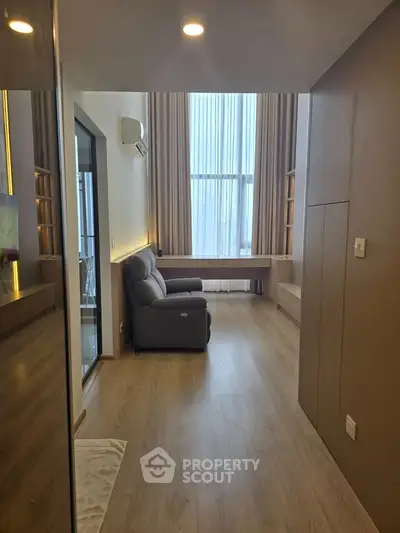 Modern living room with high ceilings and large windows, featuring a cozy armchair and sleek wooden flooring.
