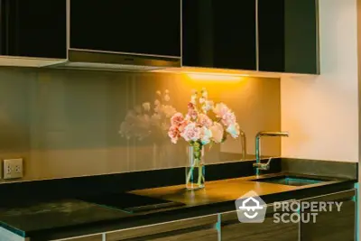 Sleek modern kitchen with dark countertops, under-cabinet lighting, and a vibrant bouquet adding a touch of elegance.