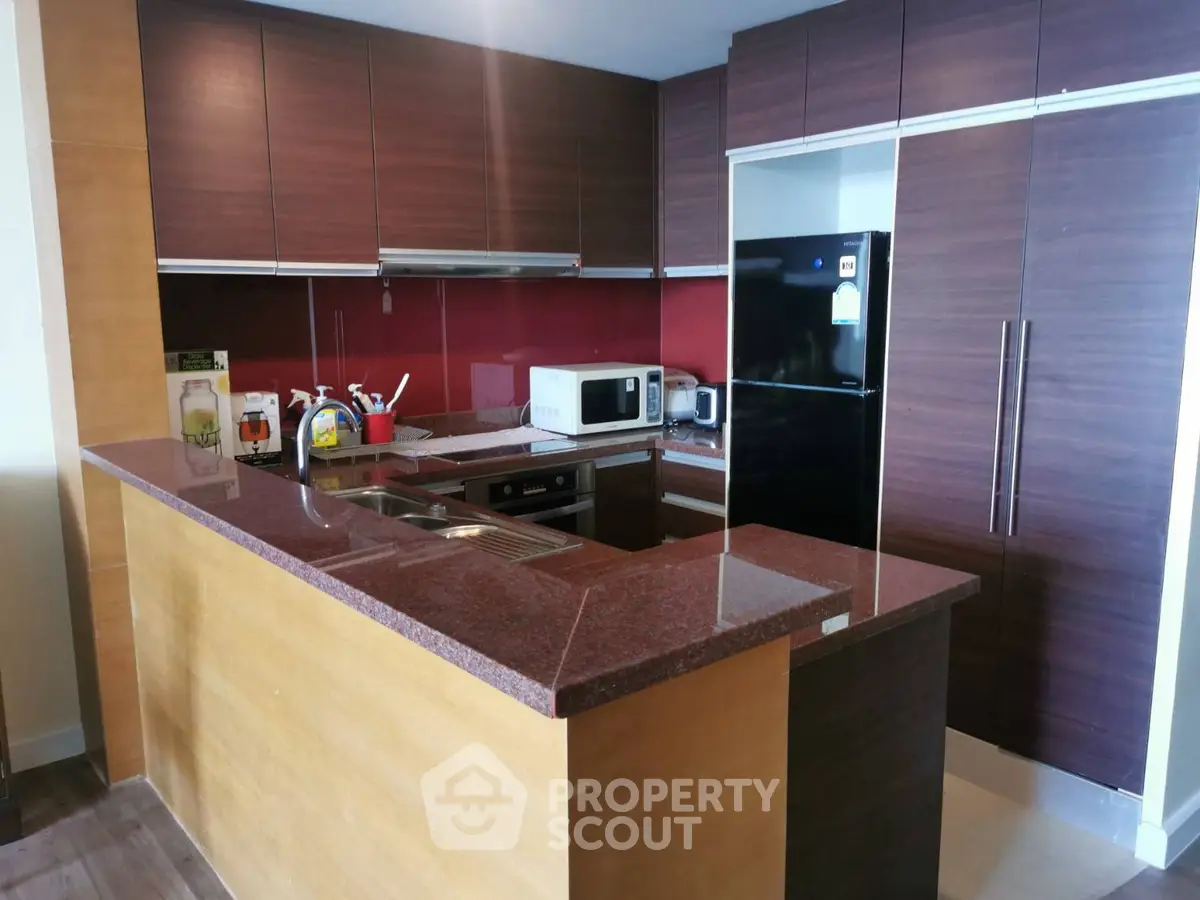 Modern kitchen with sleek cabinetry and appliances, featuring a stylish red backsplash and granite countertops.