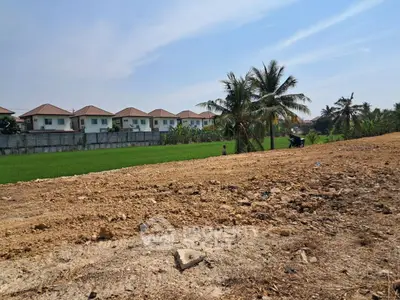Expansive land plot with potential for development near residential area and lush greenery.