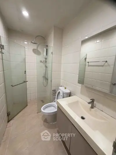 Modern bathroom with glass shower, sleek sink, and neutral tiles in a contemporary apartment.