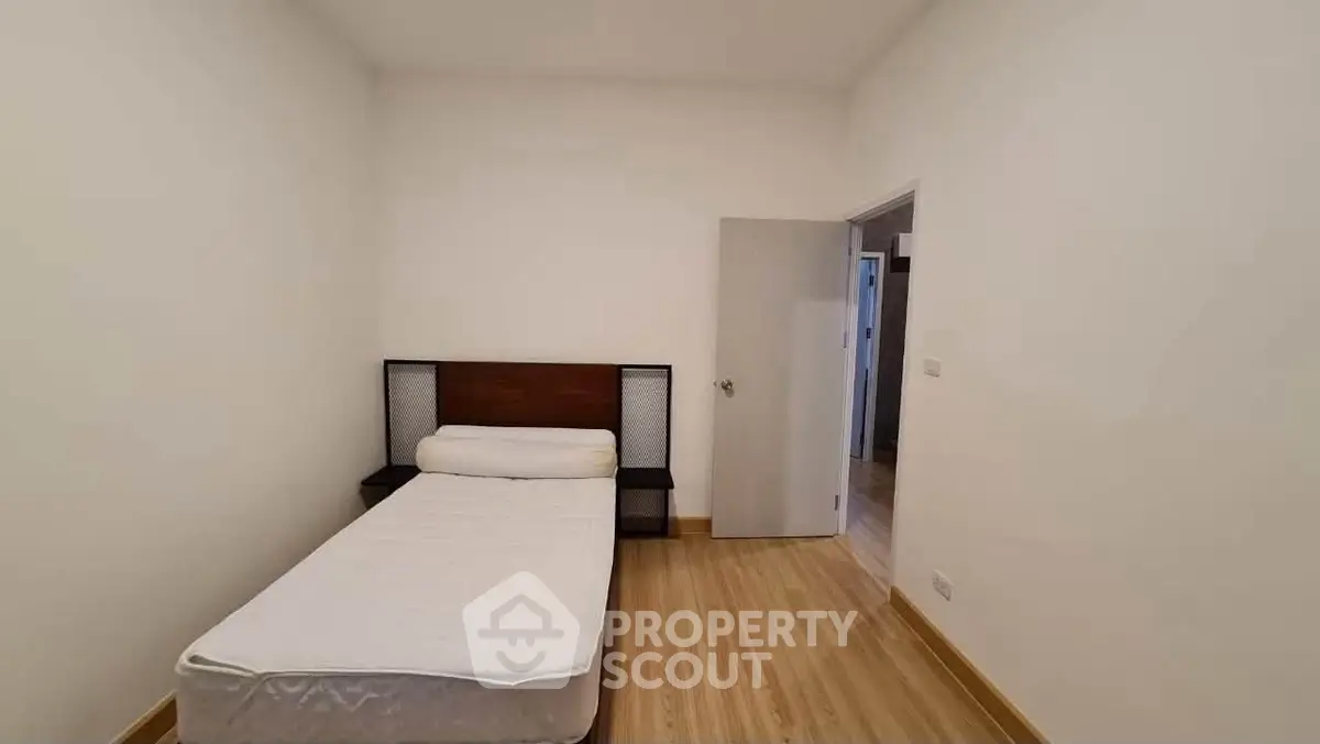 Minimalist bedroom with single bed and wooden flooring in modern apartment.