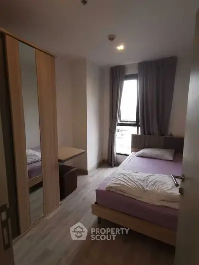 Cozy bedroom with modern furnishings and large window offering natural light.