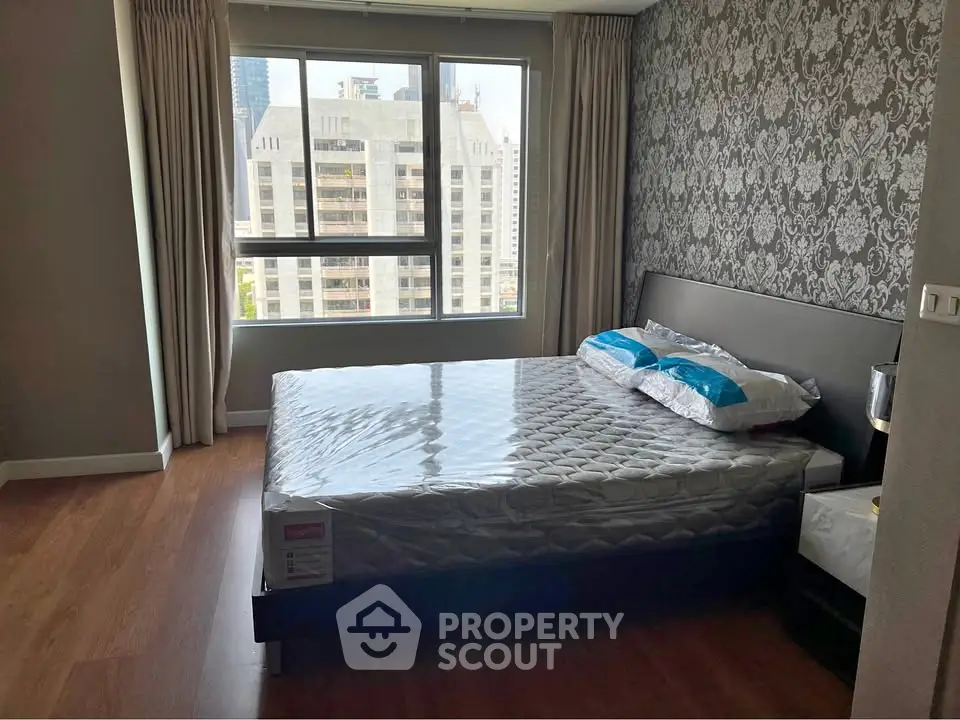 Spacious bedroom with elegant wallpaper and large window offering city views.