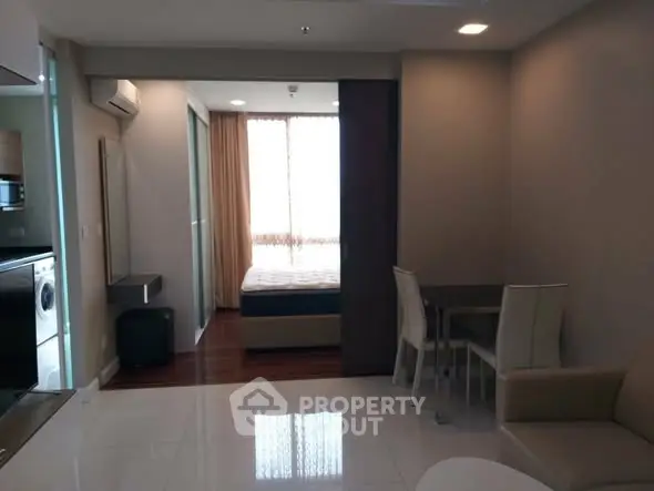 Modern open-plan living room with dining area and view into bedroom, featuring sleek furniture.