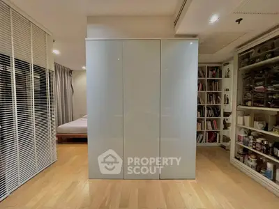 Modern bedroom with sleek wardrobe and wooden flooring, featuring a cozy reading nook with bookshelves.