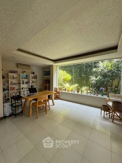 Spacious living room with large windows overlooking lush garden, featuring modern furniture and ample natural light.