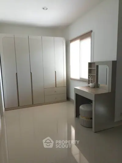 Spacious bedroom with modern wardrobe and vanity set, featuring sleek design and ample natural light.