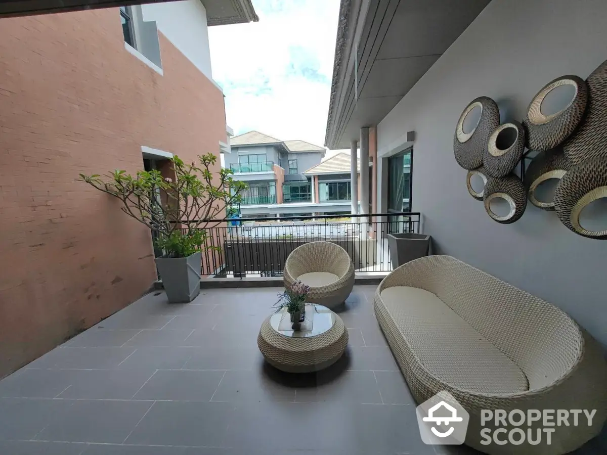 Spacious balcony with modern wicker furniture overlooking a tranquil residential area, perfect for outdoor relaxation and entertainment.