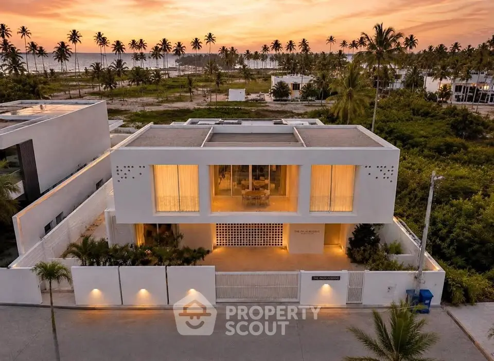 Stunning modern beachfront villa with panoramic ocean views and lush palm surroundings at sunset.