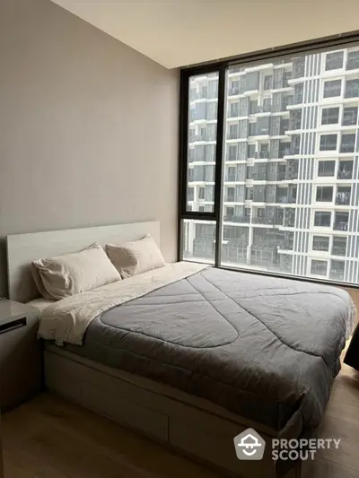 Modern bedroom with large window offering city view in high-rise apartment.