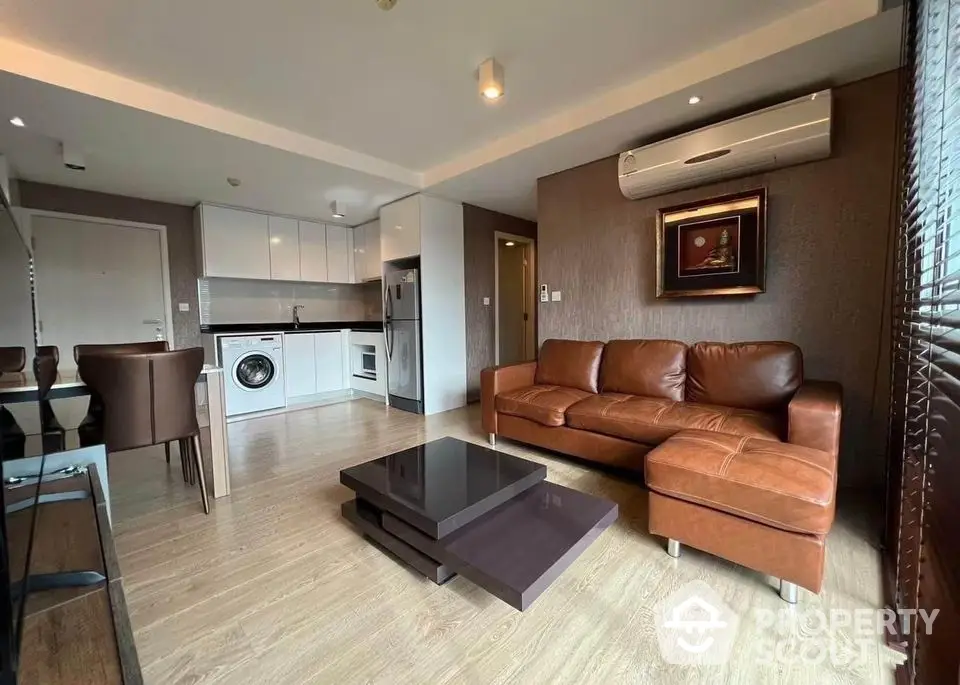 Modern living room with leather sofa and open kitchen layout in stylish apartment.