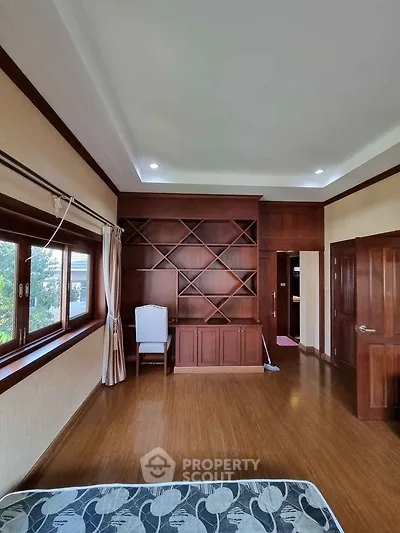 Spacious bedroom with wooden flooring and built-in shelving, large window for natural light.