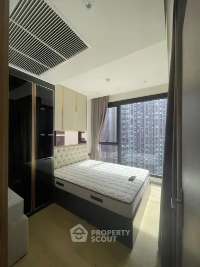 Modern bedroom with large window and city view, featuring stylish furniture and natural light.