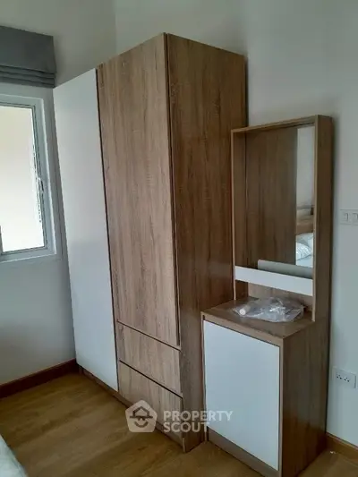 Modern bedroom with sleek wooden wardrobe and matching dresser, featuring a minimalist design and natural light.