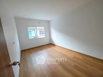 Spacious empty room with wooden flooring and bright natural light from window.
