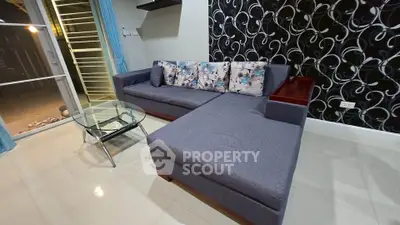 Modern living room with stylish L-shaped sofa and glass coffee table, featuring elegant wallpaper and tiled flooring.