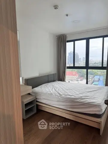 Modern bedroom with large window offering city view, featuring a cozy bed and wooden flooring.