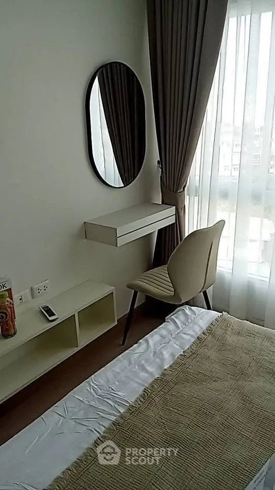 Cozy bedroom with modern decor, featuring a stylish chair, mirror, and natural light from large window.