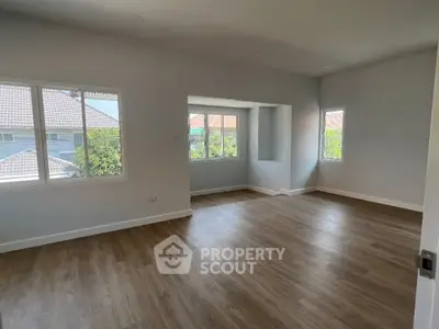 Spacious living room with abundant natural light, hardwood floors, and a serene neighborhood view, perfect for modern living.