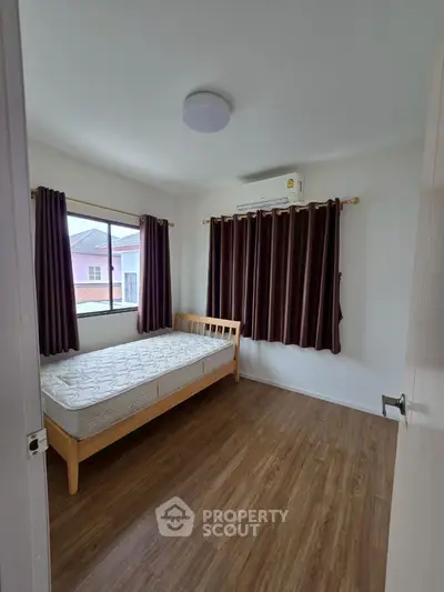 Cozy bedroom with wooden flooring and large window, featuring a single bed and air conditioning.