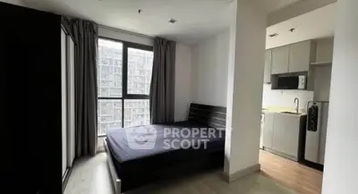 Modern bedroom with large window and adjacent compact kitchen in urban apartment.