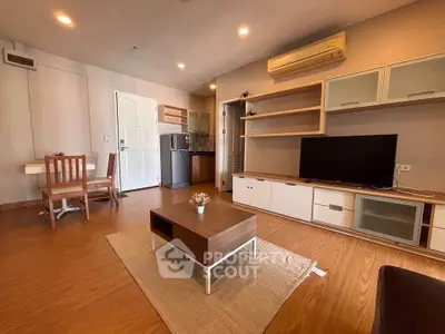 Modern living room with wooden flooring, stylish furniture, and open kitchen layout.