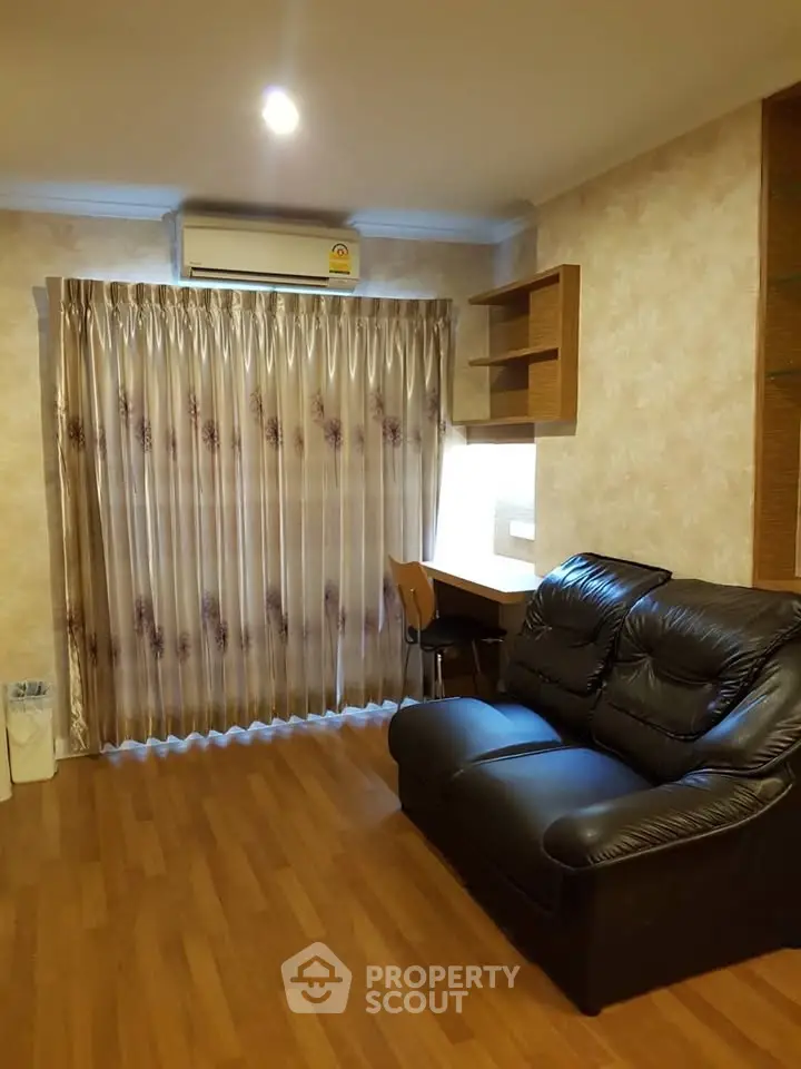 Cozy living room with leather sofa and wooden flooring, featuring elegant curtains and a compact study area.