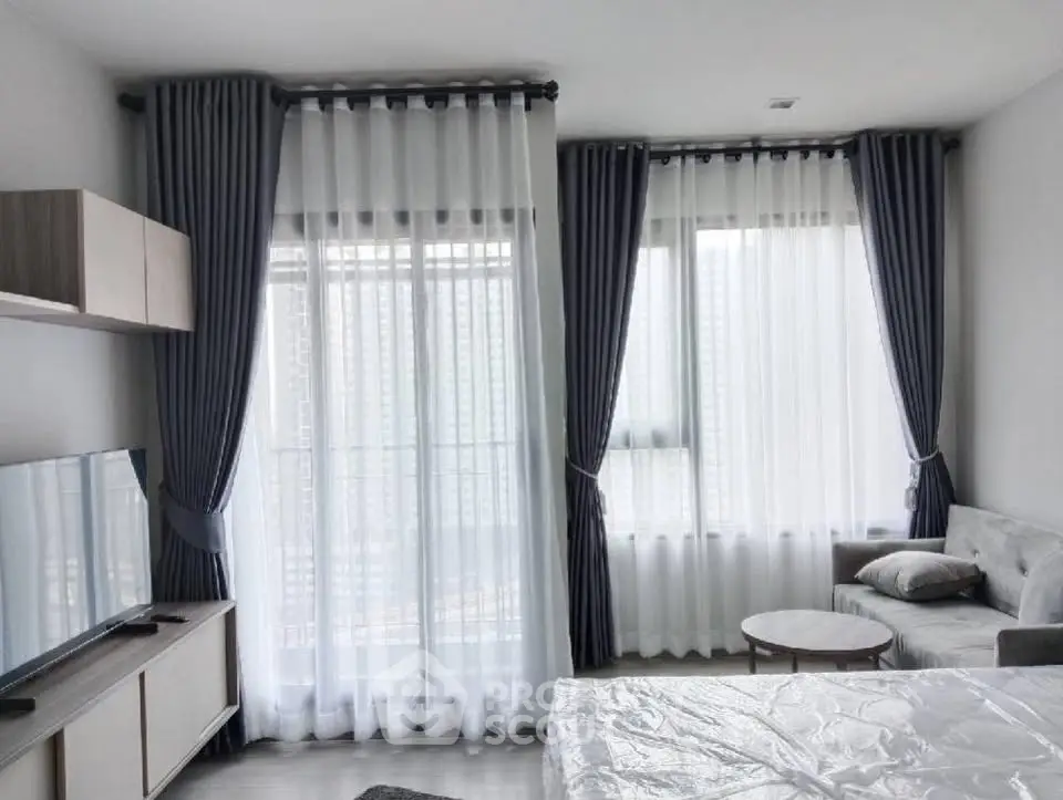 Modern living room with large windows and elegant curtains, featuring a cozy sofa and sleek TV setup.