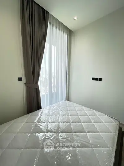 Modern bedroom with large window and elegant curtains, featuring a cozy mattress.