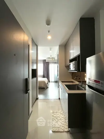Modern compact kitchen with sleek cabinetry leading to a cozy bedroom in a stylish apartment.
