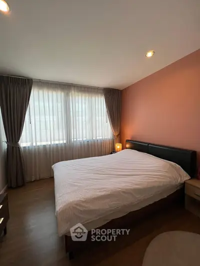 Cozy bedroom with large window and elegant curtains, featuring a comfortable bed and warm lighting.