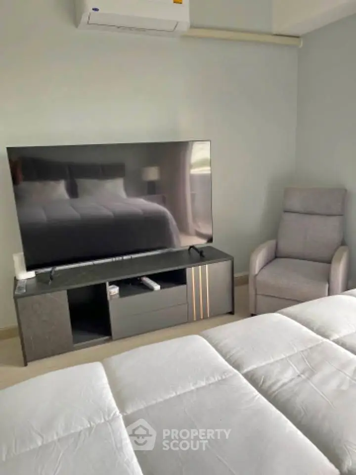 Modern bedroom with sleek TV setup and cozy armchair, perfect for relaxation.