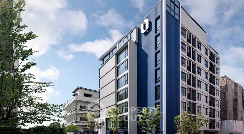 Modern blue and white apartment building with lush greenery and clear sky.