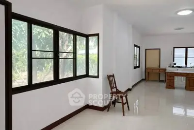 Spacious interior with large windows and natural light, featuring a simple wooden chair and desk.