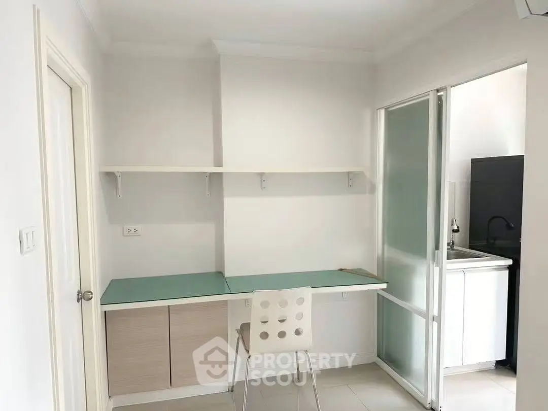 Modern study room with sleek desk and chair, adjacent to a compact kitchen area.